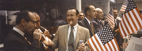 A group of NASA and Manned Space Center officials join in with the flight controllers in the Mission Operations Control Room in the Mission Control Center.