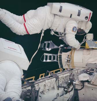 Photographic documentation showing Mission Specialist (MS) S. David Griggs, in an Extravehicular Mobility Unit (EMU) with red stripes and MS Jeffrey A.  Hoffman, in an EMU, working on attaching tools to the end effector of the  Remote Manipulator System (RMS).