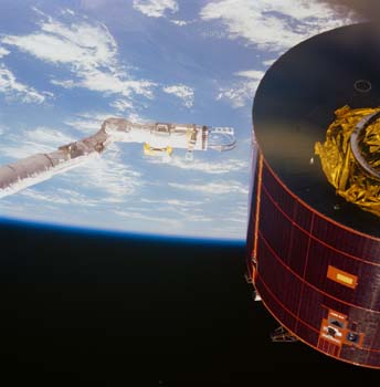 The Space Shuttle Discovery's Remote Manipulator System (RMS) arm and two specially designed extensions move toward the troubled Syncom-IV (LEASAT) communications satellite. Behind it the Earth's clouded surface can be seen. 
