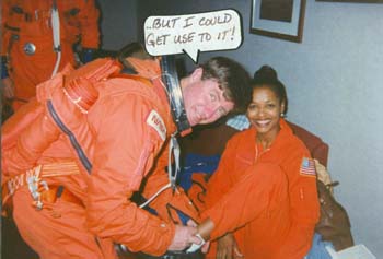 STS-78 Commnader Tom Henricks helping McDougle put on boots after she suited him up in preparation for his STA flight at the SLF at KSC. 