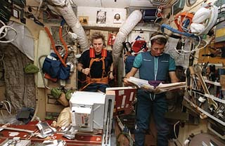 View of astronaut Shannon Lucid exercising on a treadmill in the Mir Space Station Base Block while John Blaha reviews his flight data file.